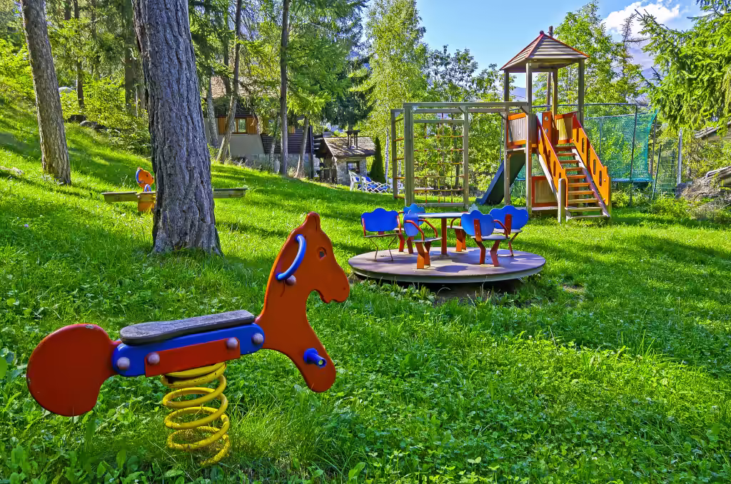 L'aire de jeux à l'ombre des arbres : tourniquet, toboggan et cheval à ressort