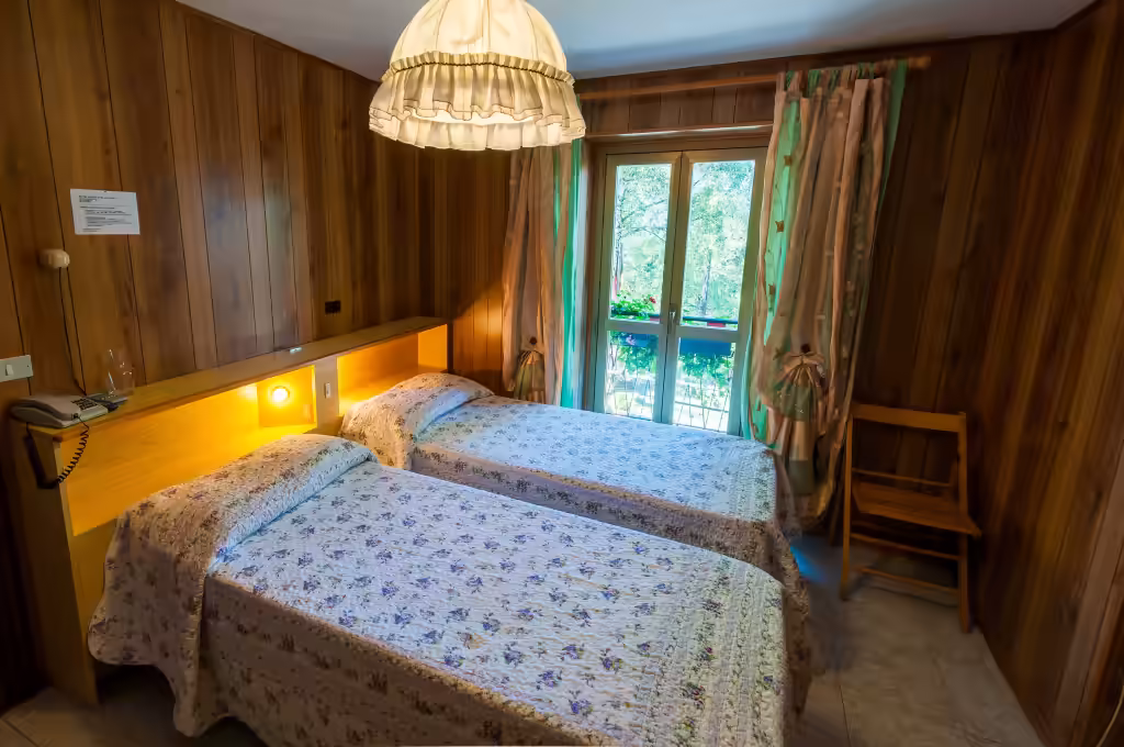Chambre à deux lits lambrissée, porte-fenêtre sur le jardin